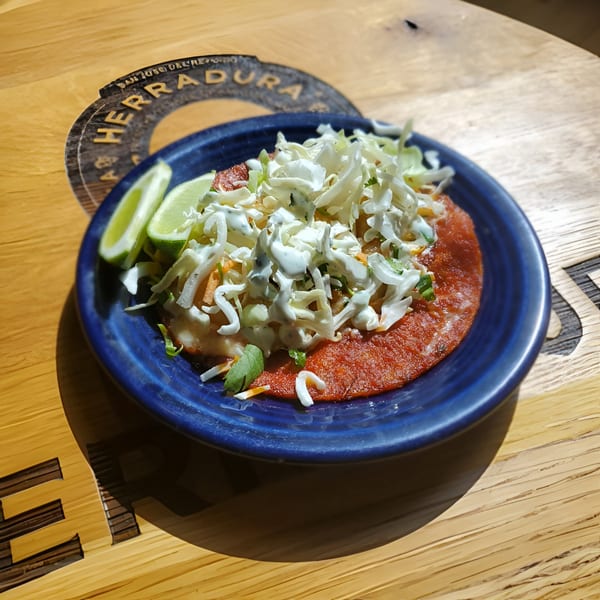 A vibrant red enchilada topped with shredded cabbage, crema, and lime wedges on a blue plate.