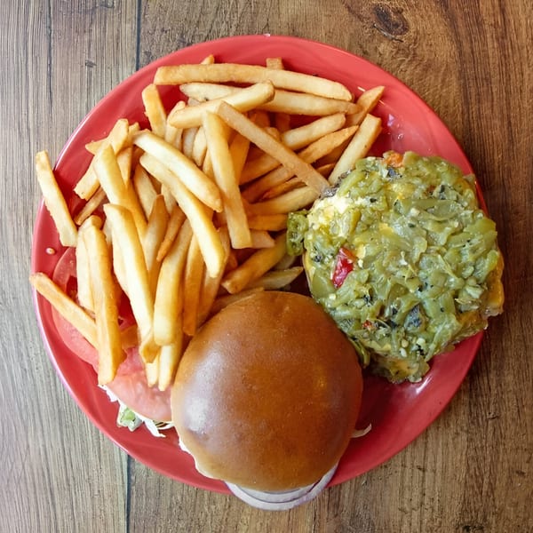 A Gazpacho Restaurant burger with green chile and fries on a red plate.
