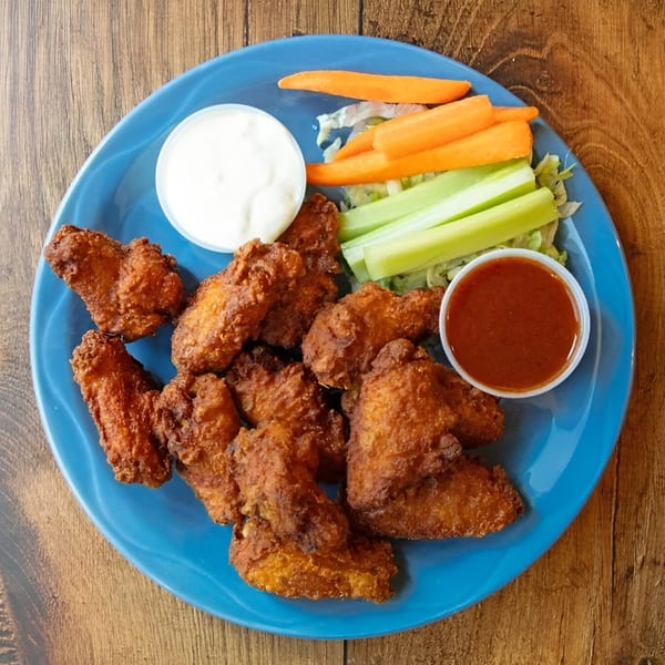 Crispy fried chicken wings with carrots, celery, ranch, and hot sauce on a blue plate.